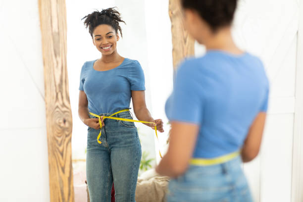 happy black girl after weight loss measuring waist at home - measuring waist imagens e fotografias de stock