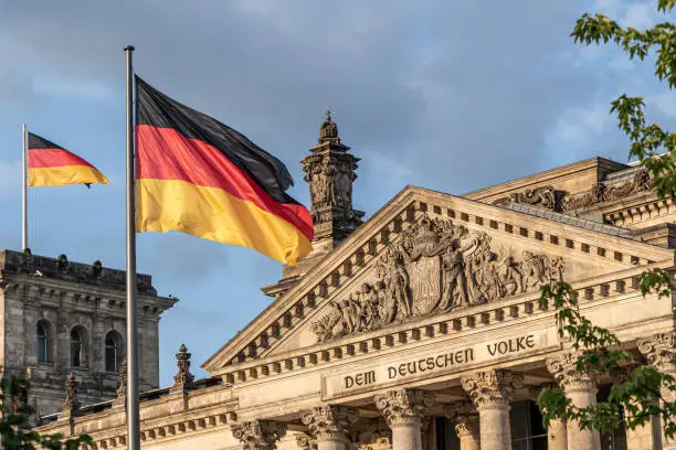 Federal Republic of Germany, German national flag at the Parliament building waving on the blue sky background, DE