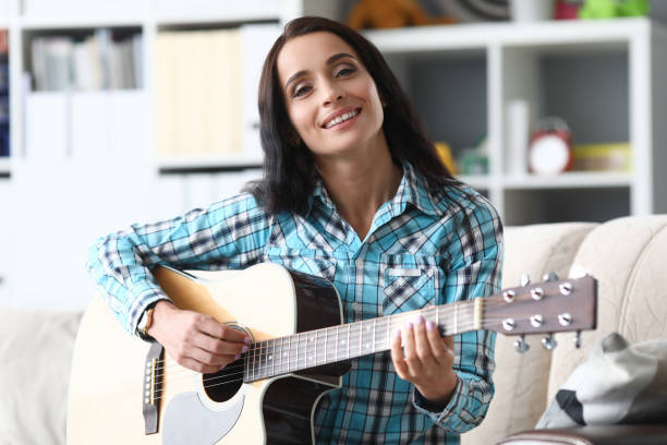 istock Woman sitting at home on sofa and playing guitar 1272976713