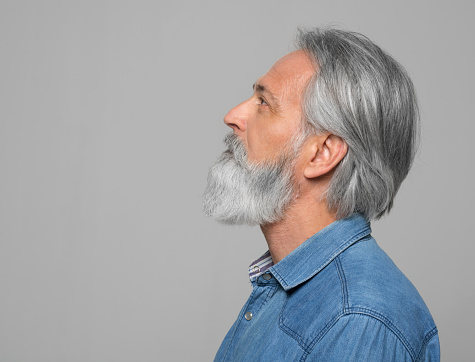Thoughtful mature man looking up while standing against grey background.