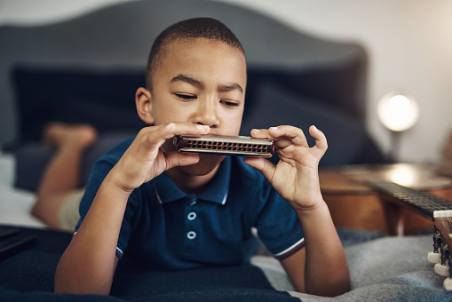 Cropped shot of a young boy playing the harmonica at home