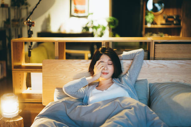 joven asiática acostada en la cama en el dormitorio, sintiéndose cansada y somnoliento, frotándose los ojos y lista para dormir por la noche - frotarse los ojos fotografías e imágenes de stock