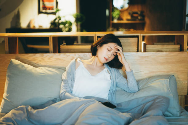 Young Asian woman feeling sick and suffering from a headache, lying on the bed and taking a rest at home Young Asian woman feeling sick and suffering from a headache, lying on the bed and taking a rest at home anemia photos stock pictures, royalty-free photos & images