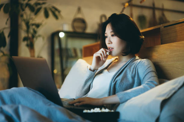 Young Asian Woman Lying On The Bed Enjoying The Weekend Watching Movie On  Laptop And Eating Popcorn At Home In The Evening Stock Photo - Download  Image Now - Istock