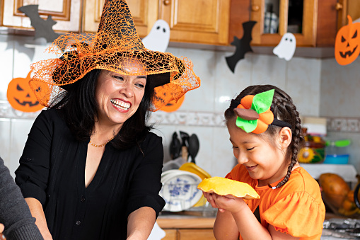 A woman with a kid wearing customs and carving a pumpkin at a decorated kitchen in Halloween