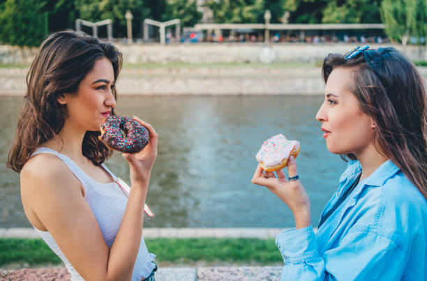 istock Two young women eating donuts 1272991883