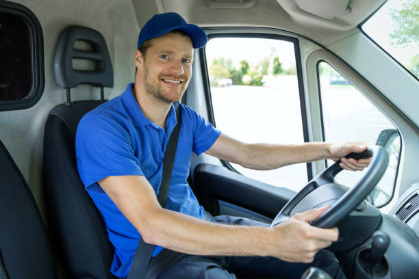 serviços de transporte - jovem motorista homem de uniforme azul dirigindo uma van. sorrindo para a câmera - driving van driver delivering - fotografias e filmes do acervo