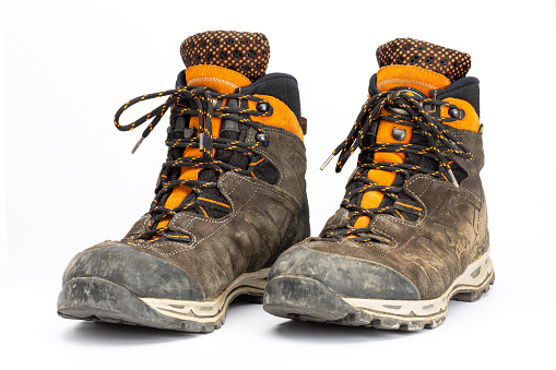 Pair of dirty brown/orange men's hiking boots with white background. Front view, landscape format.