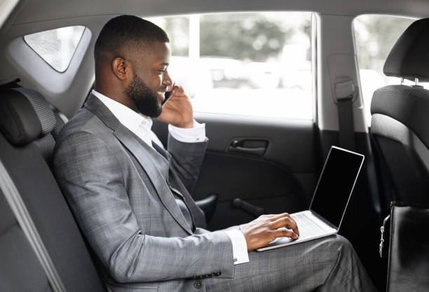 istock Young black businessman using mobile phone and laptop in car 1273001653