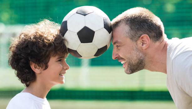 человек, держащий мяч между двумя головами с маленьким мальчиком - soccer child little boys playing стоковые фото и изображения