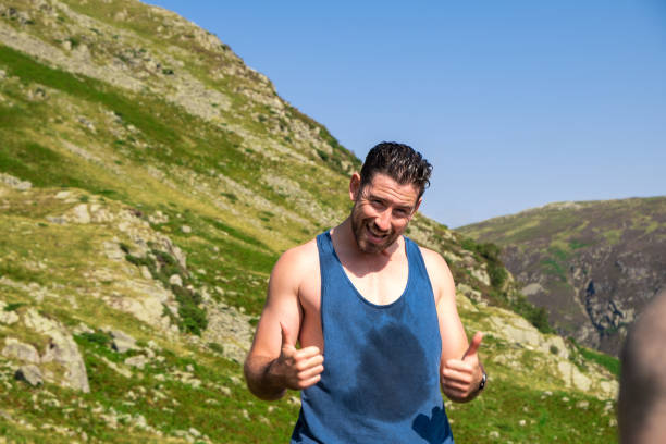 We Are Nearly At The Top A shot of a mid adult male wearing casual summery clothing with his thumbs up and looking at the camera. He is in a mountainous setting and is hot and sweaty. striding edge stock pictures, royalty-free photos & images