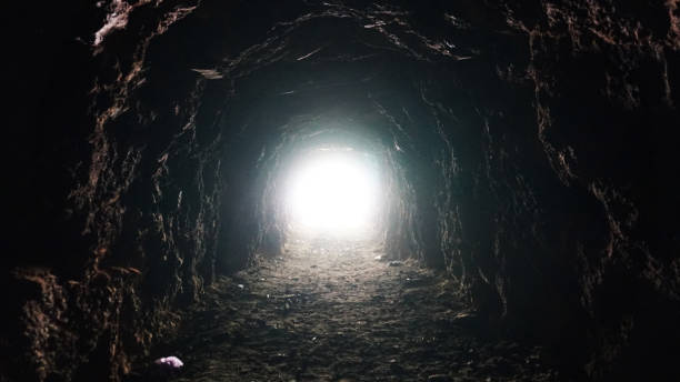 Light at the end of a long cave and children Light at the end of a long cave and children. The sunlight is bright in the eyes while in a long, dark tunnel. Children go to the exit, touching the stone walls. Rock of an artificial mine. tunnel stock pictures, royalty-free photos & images