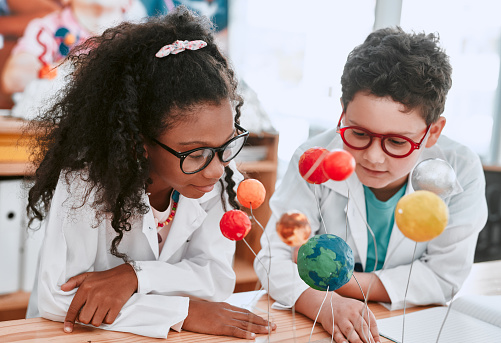 Shot of two adorable young school pupils learning about planets and the solar system in science class at school