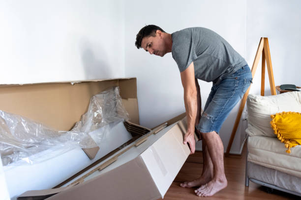 istock Moving house. Man holding and opening package of a sofa. 1273008160
