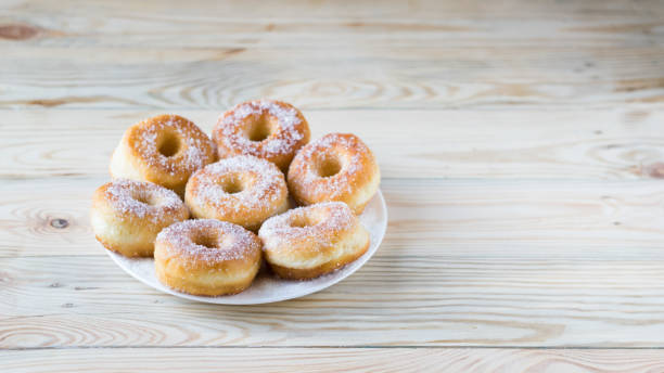 istock Homemade ring-shaped sugared donuts on a white plate on a light wooden background, rustic style, copy space 1273008833