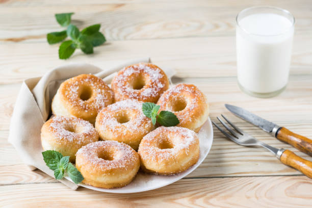 Homemade ring-shaped sugared donuts on a white plate on a light wooden background, rustic style