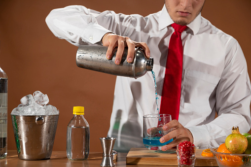 Barman preparing alcoholic drink with a cocktail shaker at the bar with some glasses of liqueur.