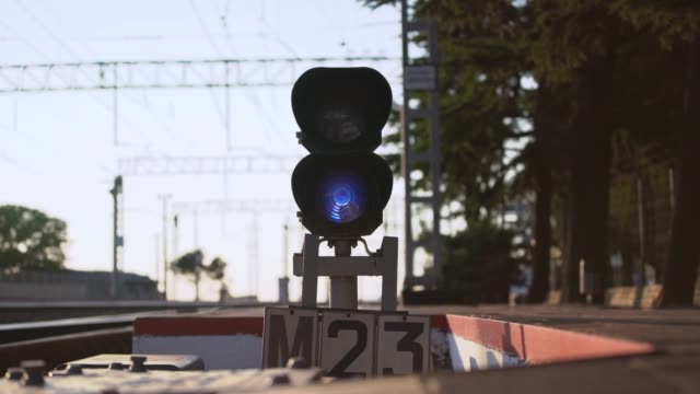 Blue sign on railway traffic light at rails end by trees
