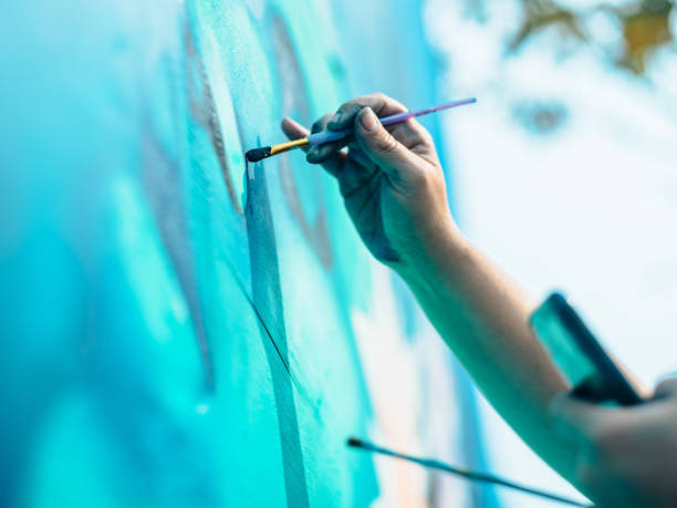 Hand of Female mural artist at work Close up of hand of Female mural artist creating art on the wall exterior in public park in the city. artists painted stock pictures, royalty-free photos & images