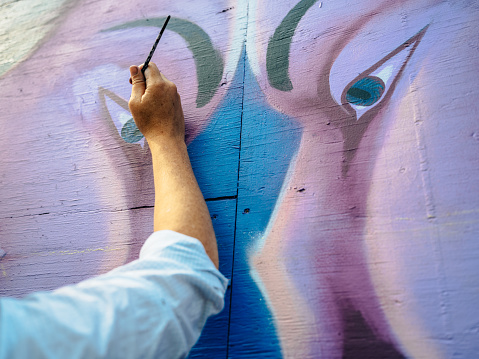 Close up of hand of Female mural artist creating art on the wall exterior in public park in the city.