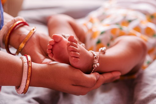 Close up Mother Holding Feet of infant Baby in Her Hand, Baby feet in mother hands. Tiny Newborn Baby's feet on female Shaped hands closeup.