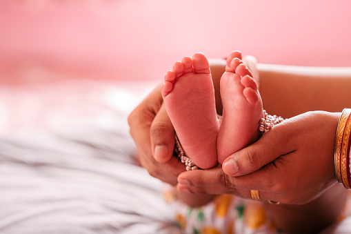 Close up Mother Holding Feet of infant Baby in Her Hand, Baby feet in mother hands. Tiny Newborn Baby's feet on female Shaped hands closeup.