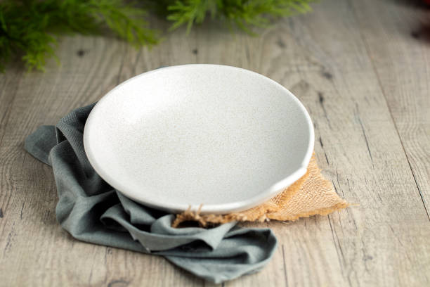 Template White deep plate on blue napkin and burlap. Wood background and green plants