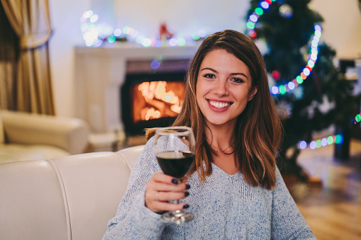 Happy woman spending New Year’s Eve at home, giving celebratory toast to friends on video call