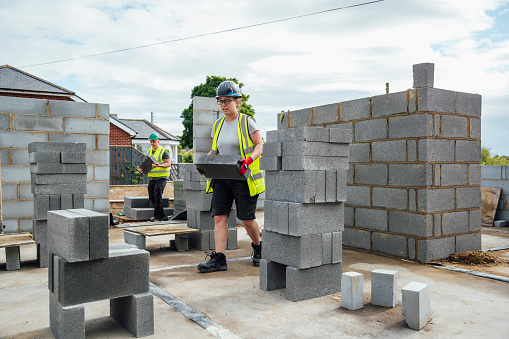 A shot of a female construction worker carrying breeze blocks on a building site with her male colleague.
