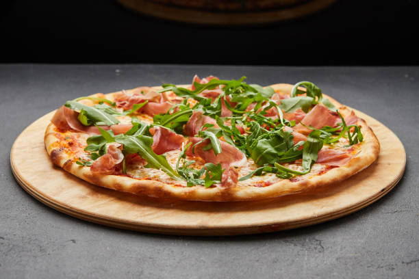 Delicious Italian Pizza with Parma ham and arugula, mozzarella cheese on dark background