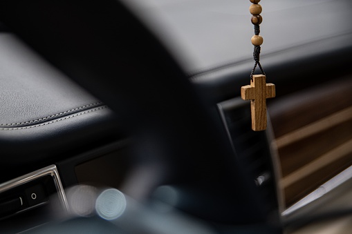 Necklace with wooden Christian cross hanging from rear mirror in car