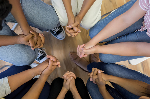 A high angle view of clasped hands of a multi-ethnic group sitting in circle.