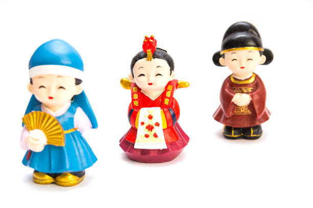 Three decorative ceramic Korean figures, two women and man, standing one by one in traditional colorful clothes Han bock isolated over a white background. Focus on the woman in red dress Three decorative ceramic Korean figures isolated korean doll stock pictures, royalty-free photos & images