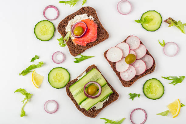 istock Appetizer, open sandwich with different toppings: salmon and vegetables on white background. Traditional Italian or Scandinavian cuisine. Healthy eating. Flat lay 1273056275