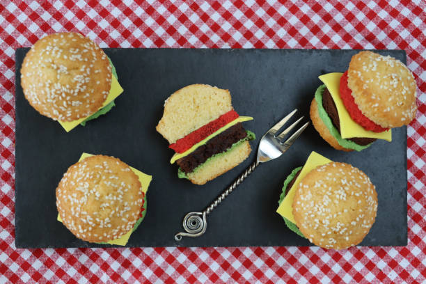 bild von schiefer-tischmat, hausgemachte schokolade und vanille cupcakes als mini-käseburger in sesam-brötchen, schwammsalat und tomate mit fondant-eiskäsescheiben, rot und weiß karierte tischdecke, erhöhte aussicht - afternoon tea place setting cupcake cake stock-fotos und bilder