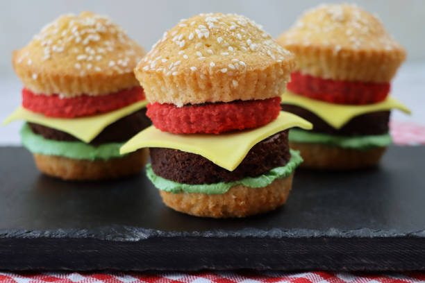 bild von schiefer-tischmat, hausgemachte schokolade und vanille cupcakes als mini-käseburger in sesam-brötchen, schwammsalat und tomate mit fondant-eiskäsescheiben, rot und weiß kariert tischdecke, fokus auf den vordergrund - afternoon tea place setting cupcake cake stock-fotos und bilder