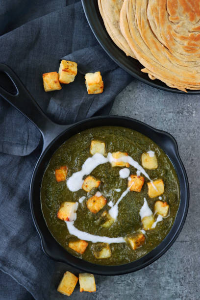 image de poêle ronde en fonte, repas végétarien palak paneer (fromage cottage, purée d’épinards) recette, tissu de fromage bleu-gris, lachha paratha (pain plat), dispersion de cubes de fromage caillé frit sur fond bleu-gris, vue surélevée - poêle verte photos et images de collection