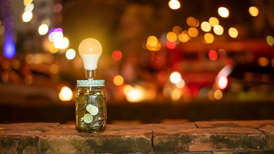 Financial long term money saving idea, piggy bank, coin and light bulb in the night with beautiful bokeh as background.