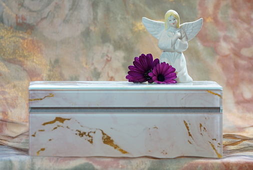 My mother my angel A beautiful white and gold funeral urn with an angel figurine on top and two purple african daisies