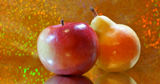 istock Close up of an apple and a pear side by side  on a mirror on a bright glittering bokeh background 1273123864