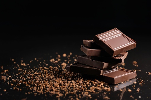 Broken pieces of chocolate with cocoa powder on a black background.
