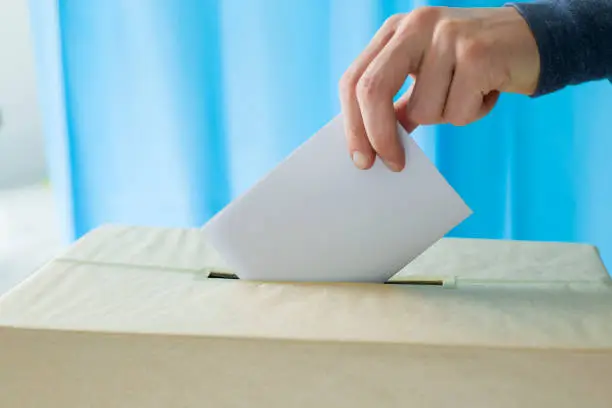 Man's hand holding a ballot paper for voting at a polling station during elections or referendum.