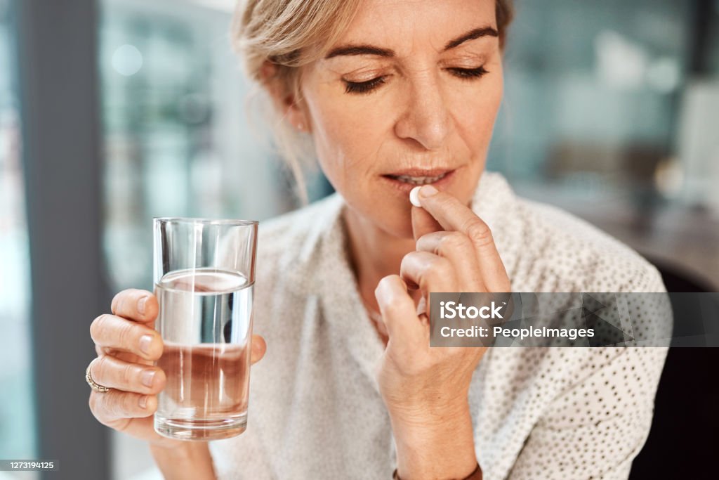 This aspirin should take care of my headache Shot of a mature businesswoman taking medication in an office Women Stock Photo