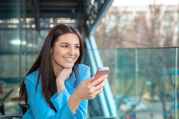 femme assise à une terrasse de café ou balcon à la maison dans l’isolement tenant téléphone portable textos quelqu’un - decisions women thinking latin american and hispanic ethnicity photos et images de collection