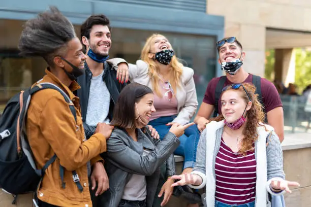 Photo of young students joking and laughing around the city wearing the protective mask under the chin, new normal socialization and new habits for the prevention of corona virus outbreak