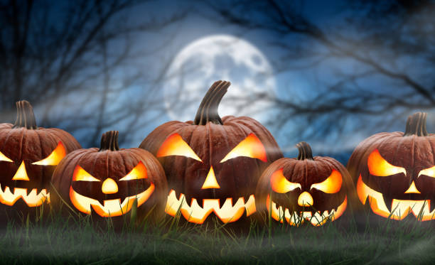 istock Five spooky halloween pumpkin, Jack O Lantern, with an evil face and eyes on the grass with a misty night sky background with a full moon. 1273198170