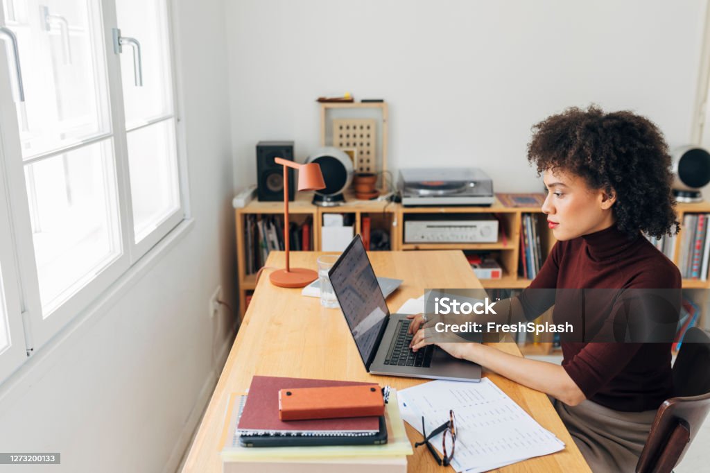 At the Home Office: African American Woman Sitting at her Desk and Working on her Laptop PC Young woman working from home, adapting to the new normal concept. Education Training Class Stock Photo