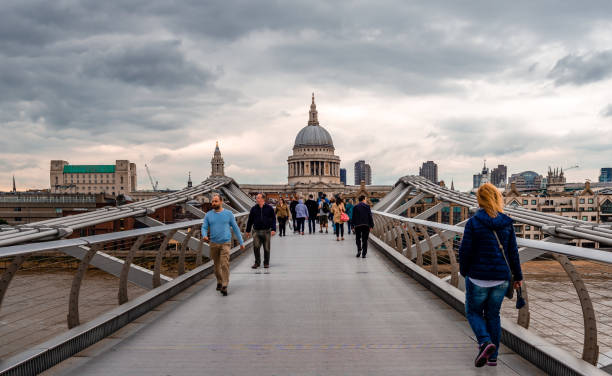 The bridge officially known as the London Millennium Footbridge, is a steel suspension bridge for pedestrians crossing the River Thames in London, England, linking Bankside with the City of London. The image shows the Millennium Bridge and St.Paul's Cathedral with many pedestrians, captured during summer seaosn.