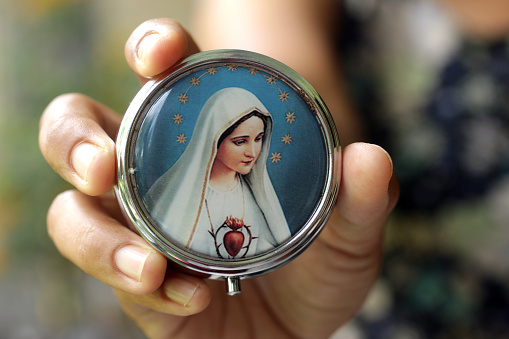 Hand holding round metal rosary box with portrait of Mother Virgin Mary on the front cover. Person showing Mother Mary picture in a rosary box. Love devotion concept with Catholic religion symbol.