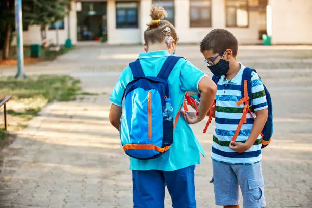 Photo of Back To School - Two Boys With Protective Face Masks In Schoolyard Talking